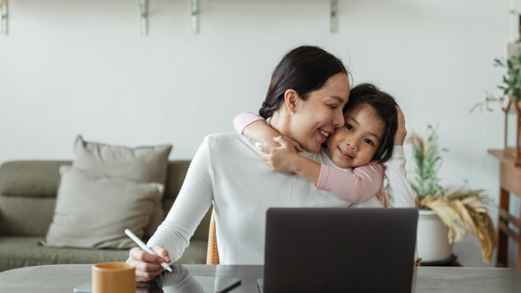 Woman working from home while hugging her daughter
